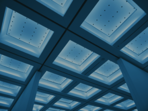 Looking up at a grid of illuminated ceiling skylights, symbolising the ceiling set above minimum compliance requirements