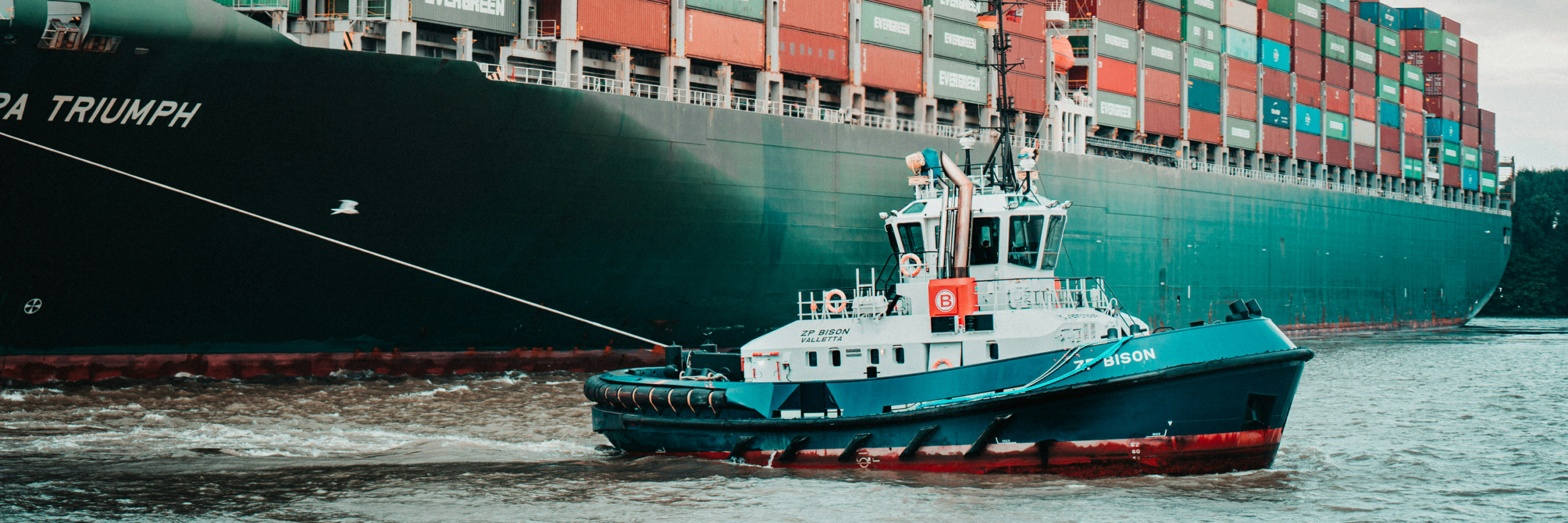 A tugboat guides a fully loaded container ship into port